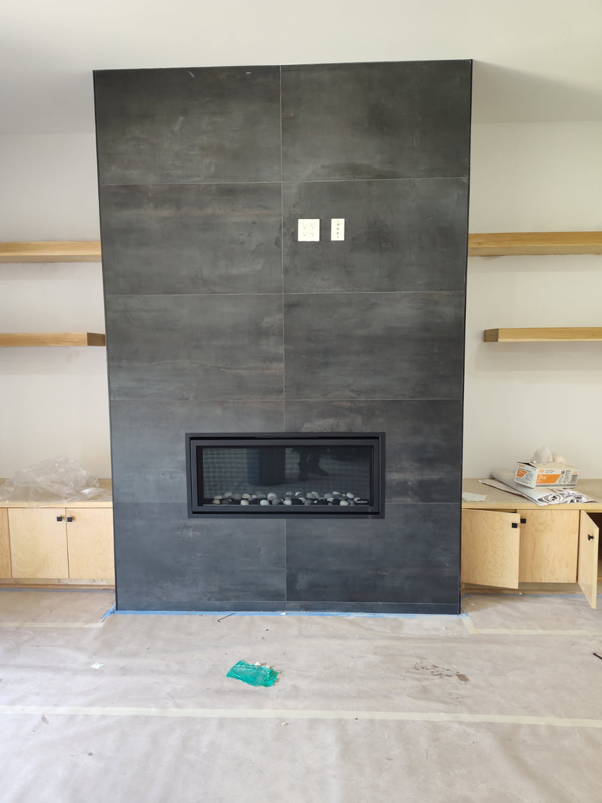 Modern linear gas fireplace clad in large-format charcoal porcelain tile with oak shelving in Houston, TX