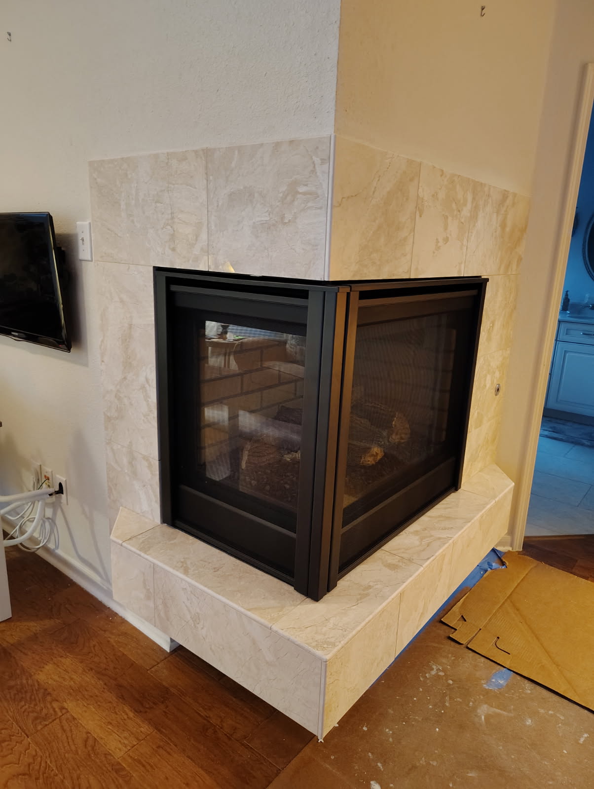 Corner see-through gas fireplace wrapped in travertine tile in Cypress, TX