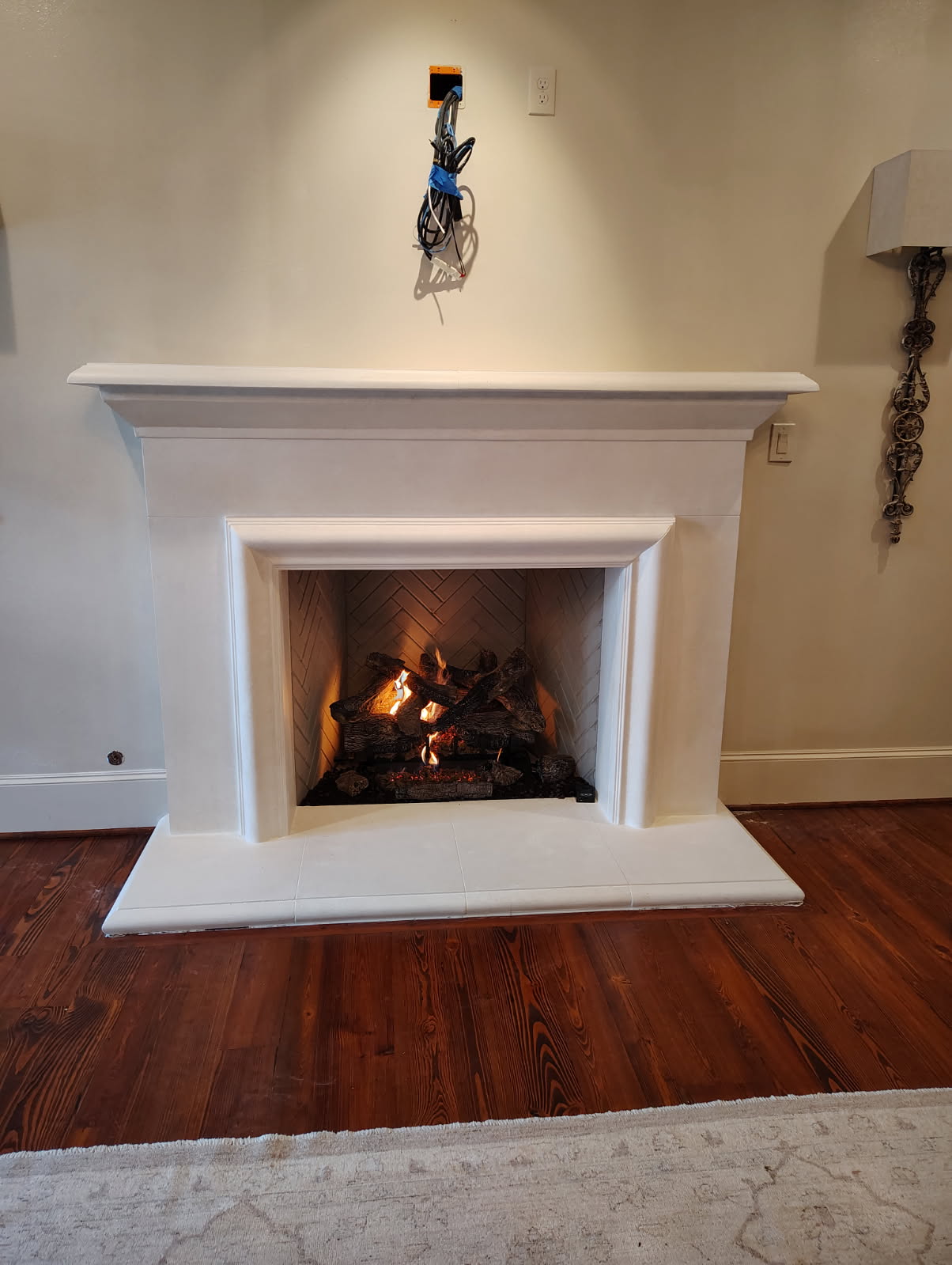 Cast stone mantel and surround over a herringbone firebox with gas logs burning in Houston, TX