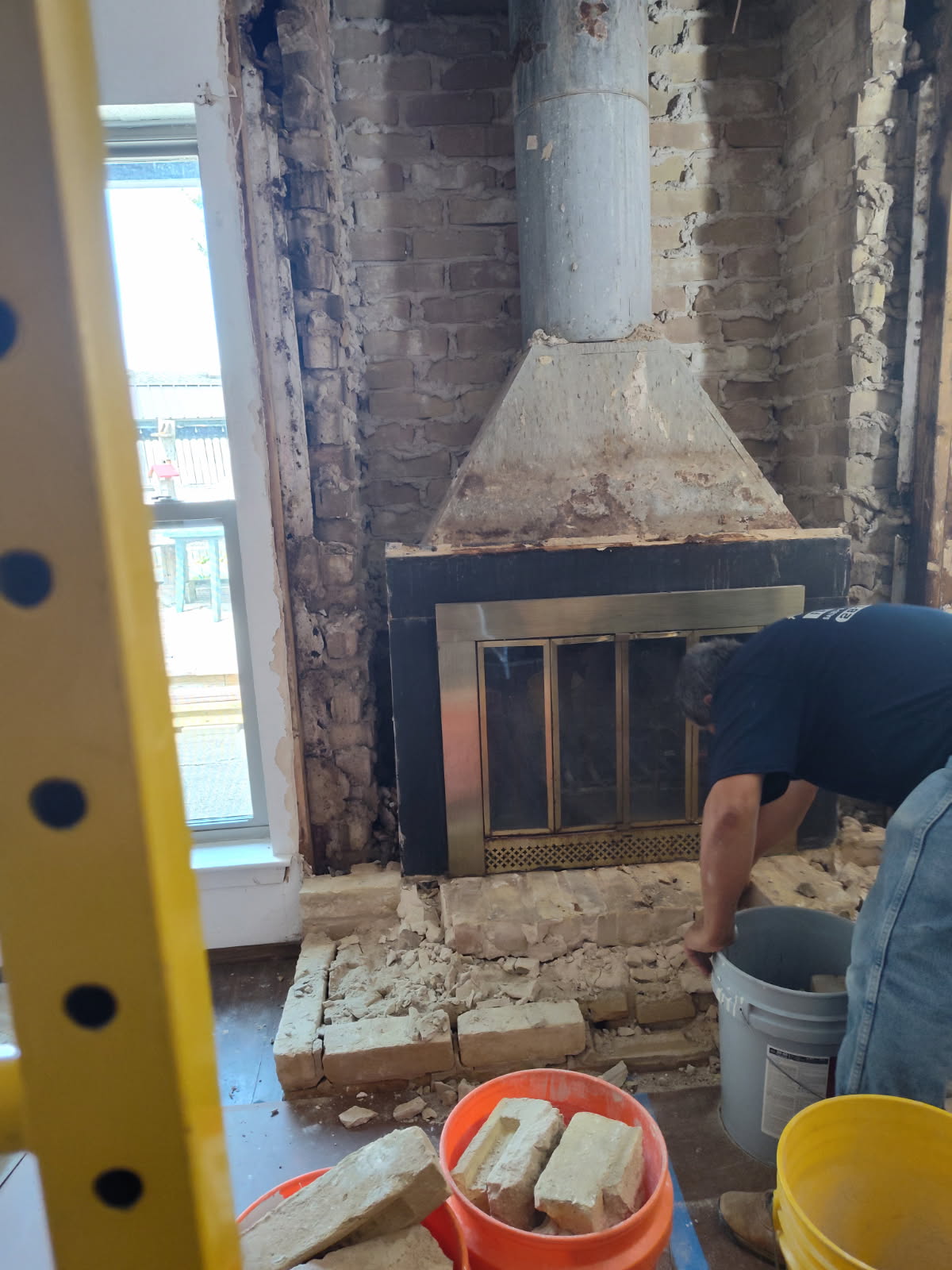 Mason demolishing an old brick firebox and hearth during a fireplace tear-out in Houston, TX